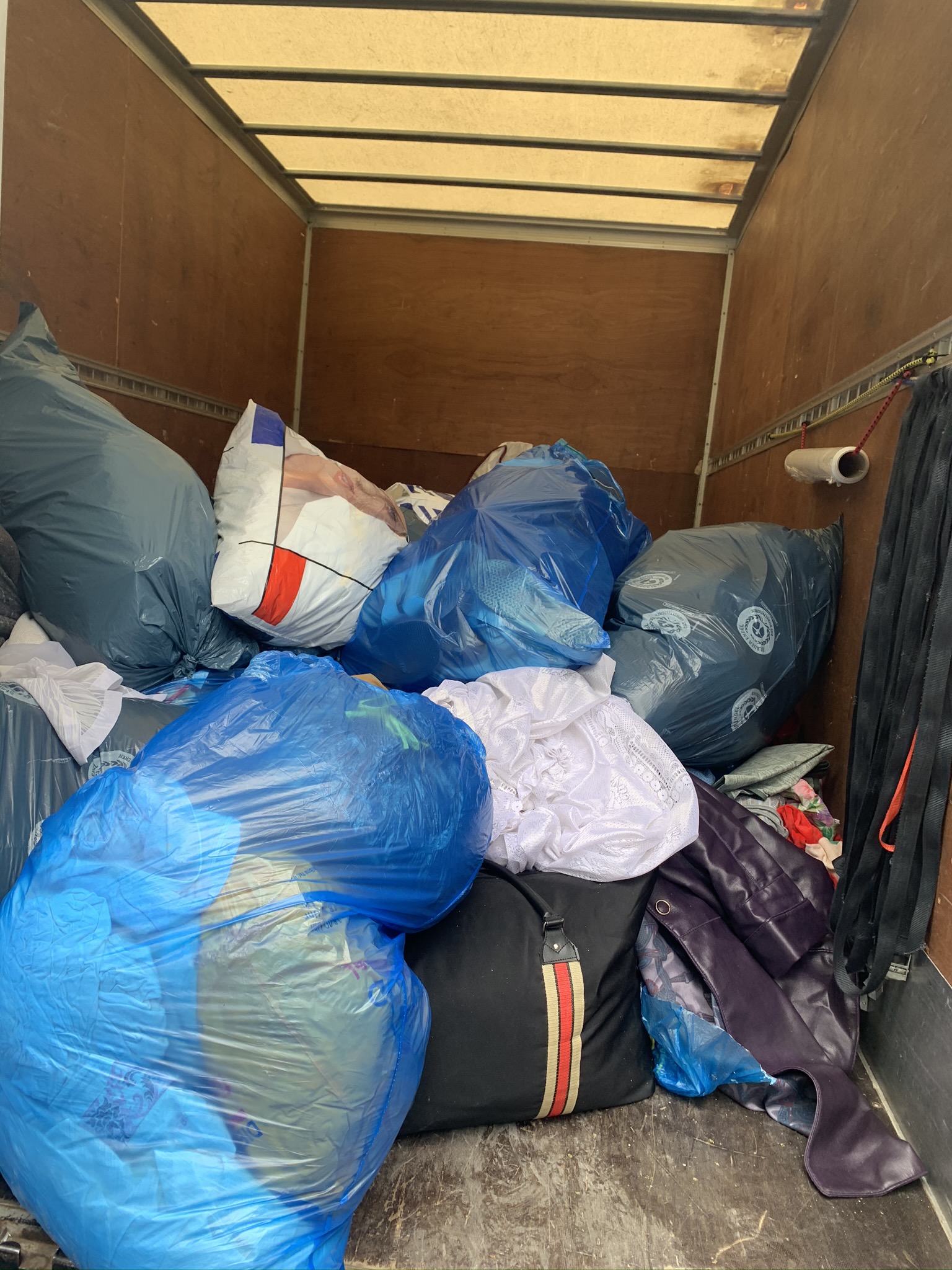 Blaue und schwarze, mit Gegenständen gefüllte Säcke liegen im hinteren Bereich eines leeren Umzugswagens.