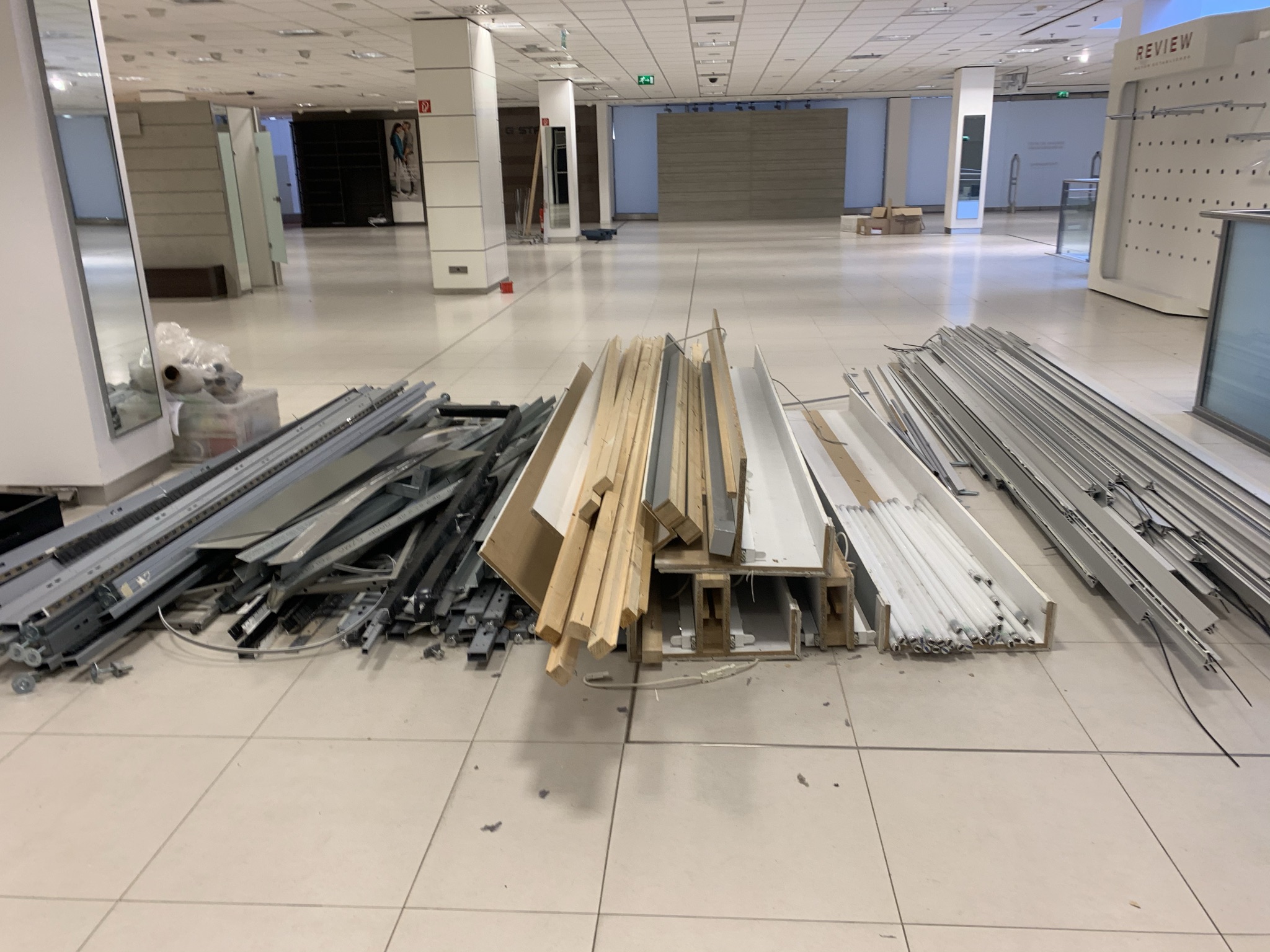 Metall- und Holzbalken, Platten und Rahmen sind ordentlich auf dem Boden in einer großen, leeren Gewerbefläche gestapelt.